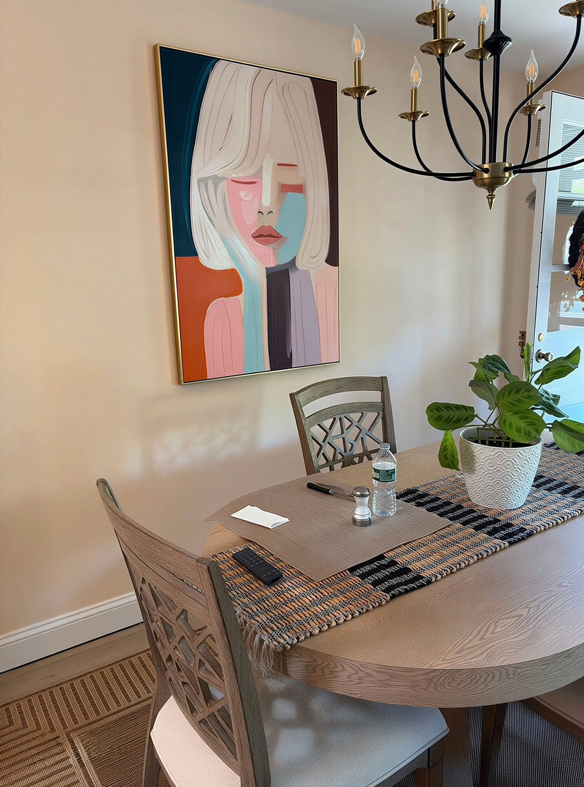 A large framed abstract portrait painting hangs on a beige wall above a dining table.