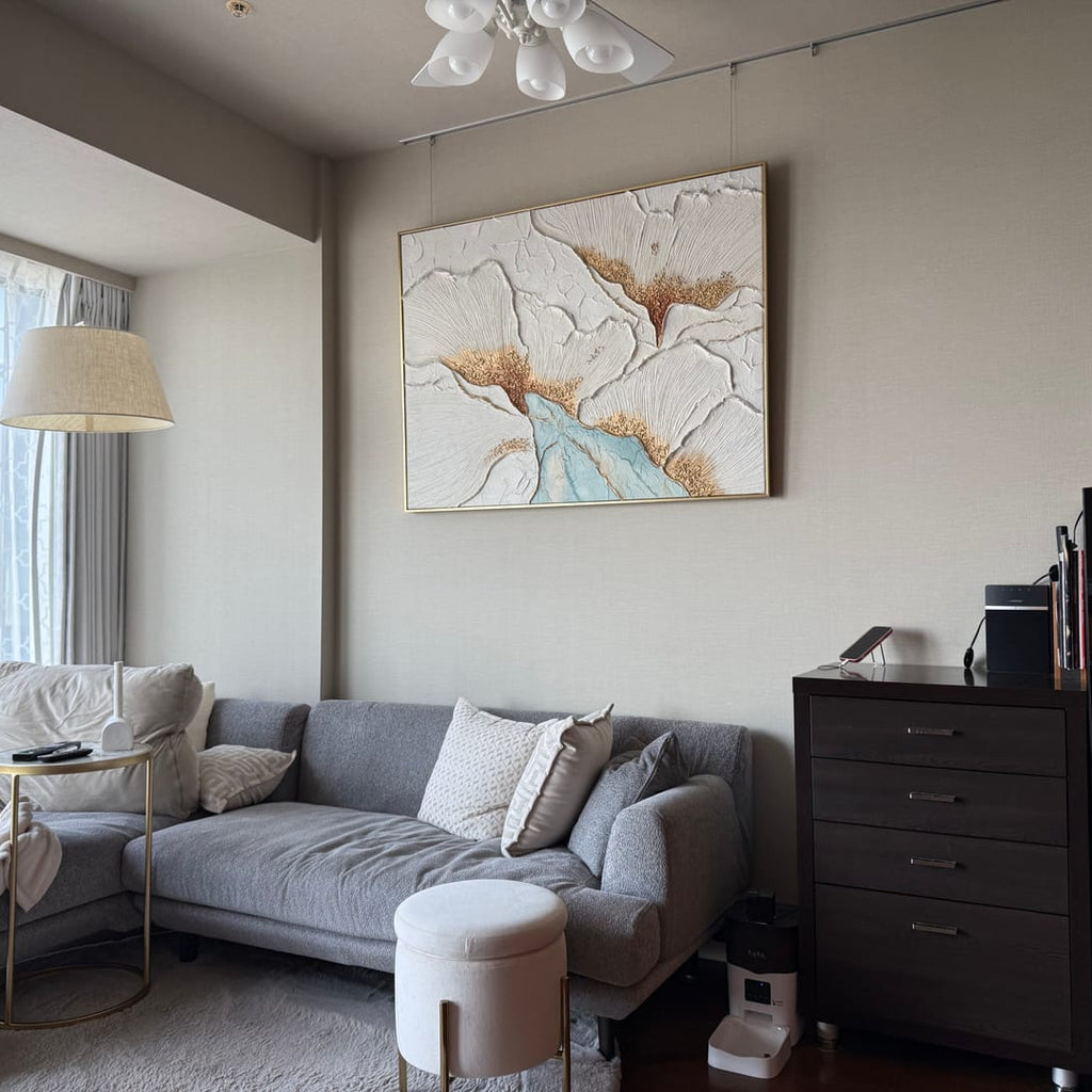 A gold floral textured wall art piece hangs above the living room sofa.