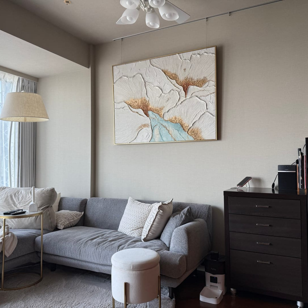 A gold floral textured wall art piece hangs above the living room sofa.
