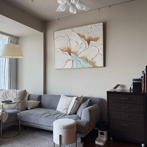 A gold floral textured wall art piece hangs above the living room sofa.