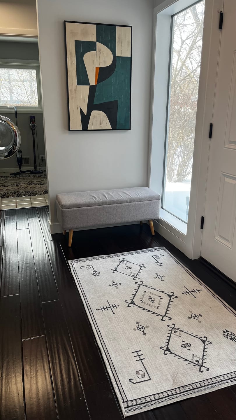 A large, abstract geometric plaster wall painting in beige and green hangs on a chair in the entryway.