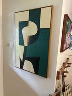A large abstract geometric wall art painting with a textured, raised canvas surface, featuring blocks of teal, cream, black, and a small orange accent, framed in a light wood border and hung on a white wall.