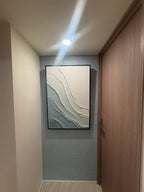 A large framed wabi sabi abstract wall art print with flowing white and gray textured lines, displayed on a light blue-gray tiled wall in a hallway.