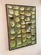 An abstract framed painting featuring textured, rounded shapes in muted olive green, beige, and brown tones, hung on a living room wall.