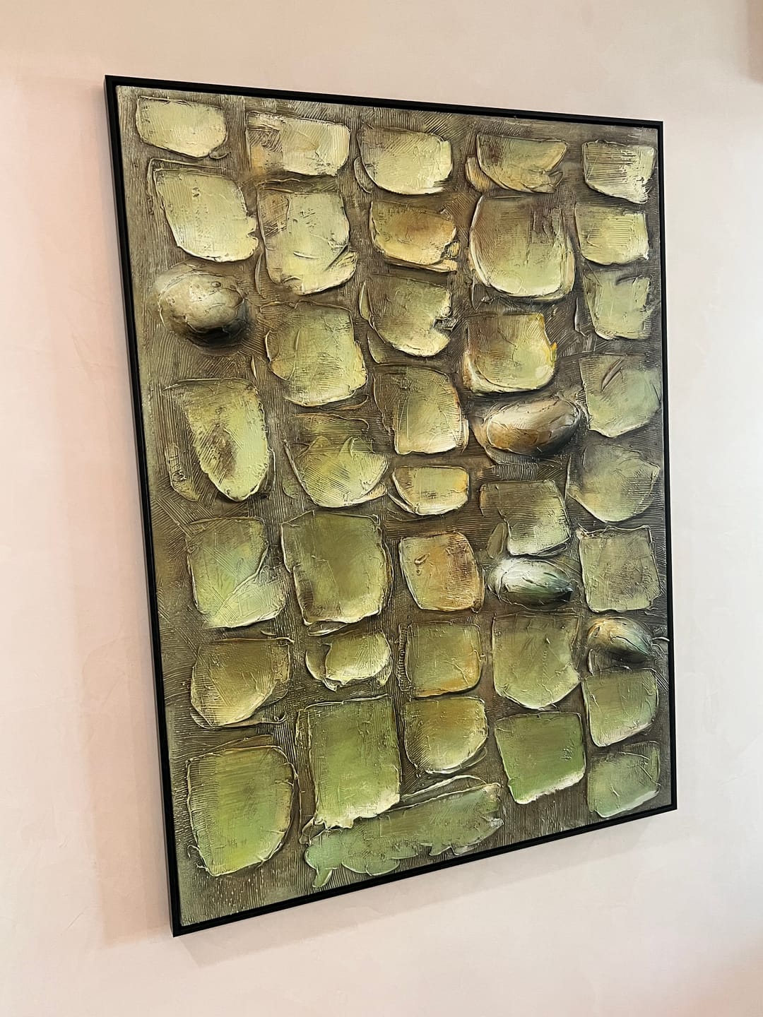 An abstract framed painting featuring textured, rounded shapes in muted olive green, beige, and brown tones, hung on a living room wall.