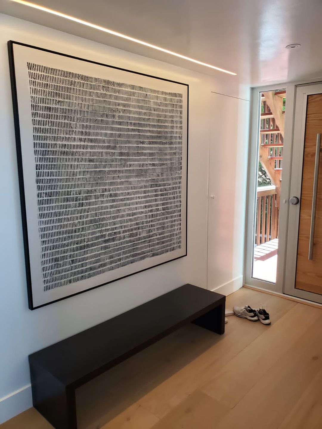 A large framed black and white abstract art print hangs on a porch stool in a modern entryway.