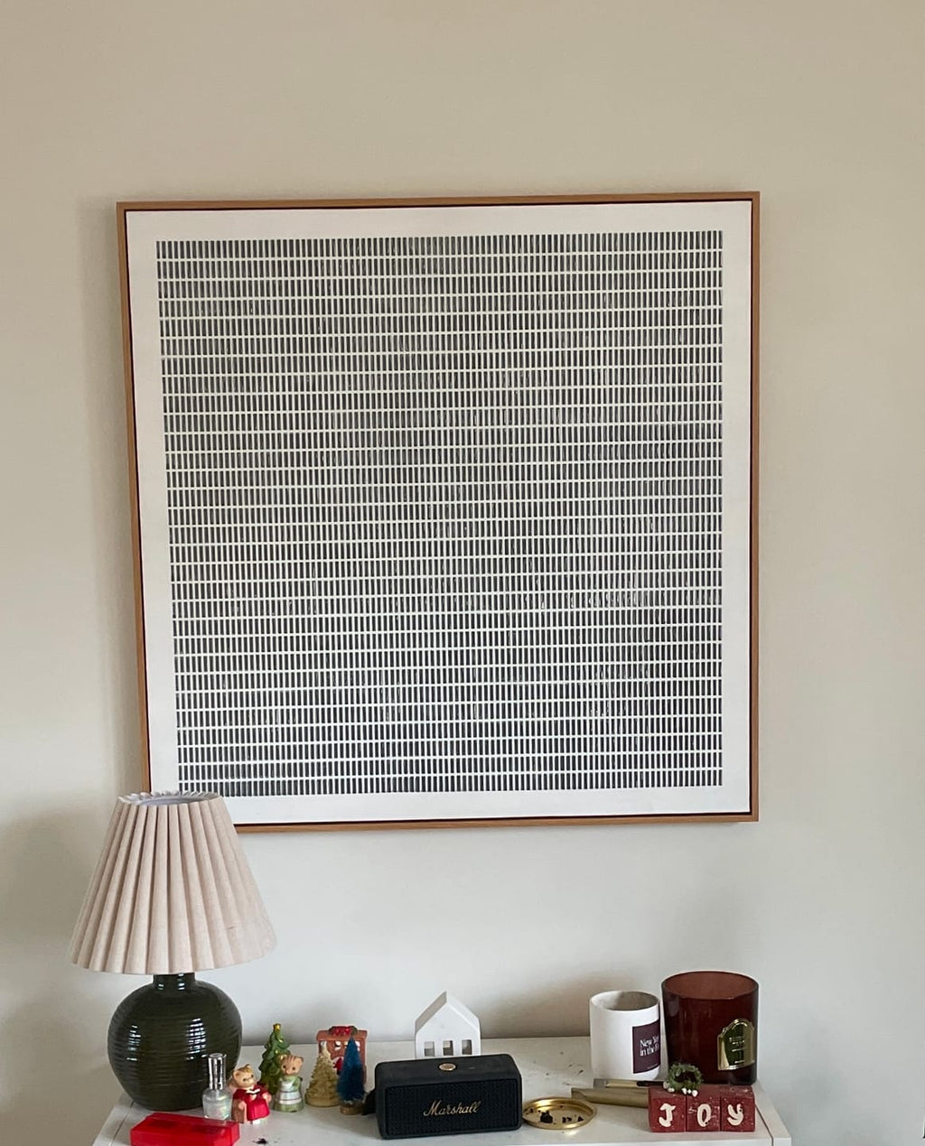 A large framed minimalist square art print featuring a black and white grid pattern above a console table.