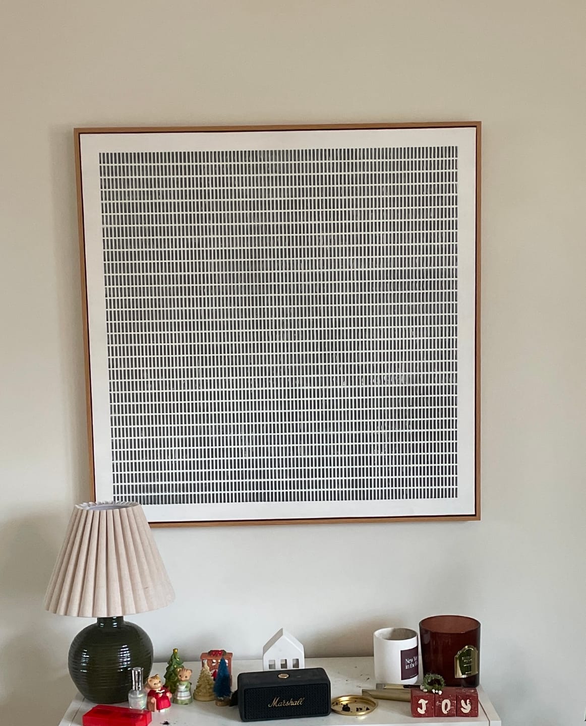 A large framed minimalist square art print featuring a black and white grid pattern above a console table.