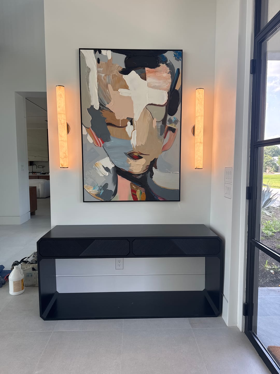 An abstract, colorful, textured portrait painting hangs above a stool in the entryway.