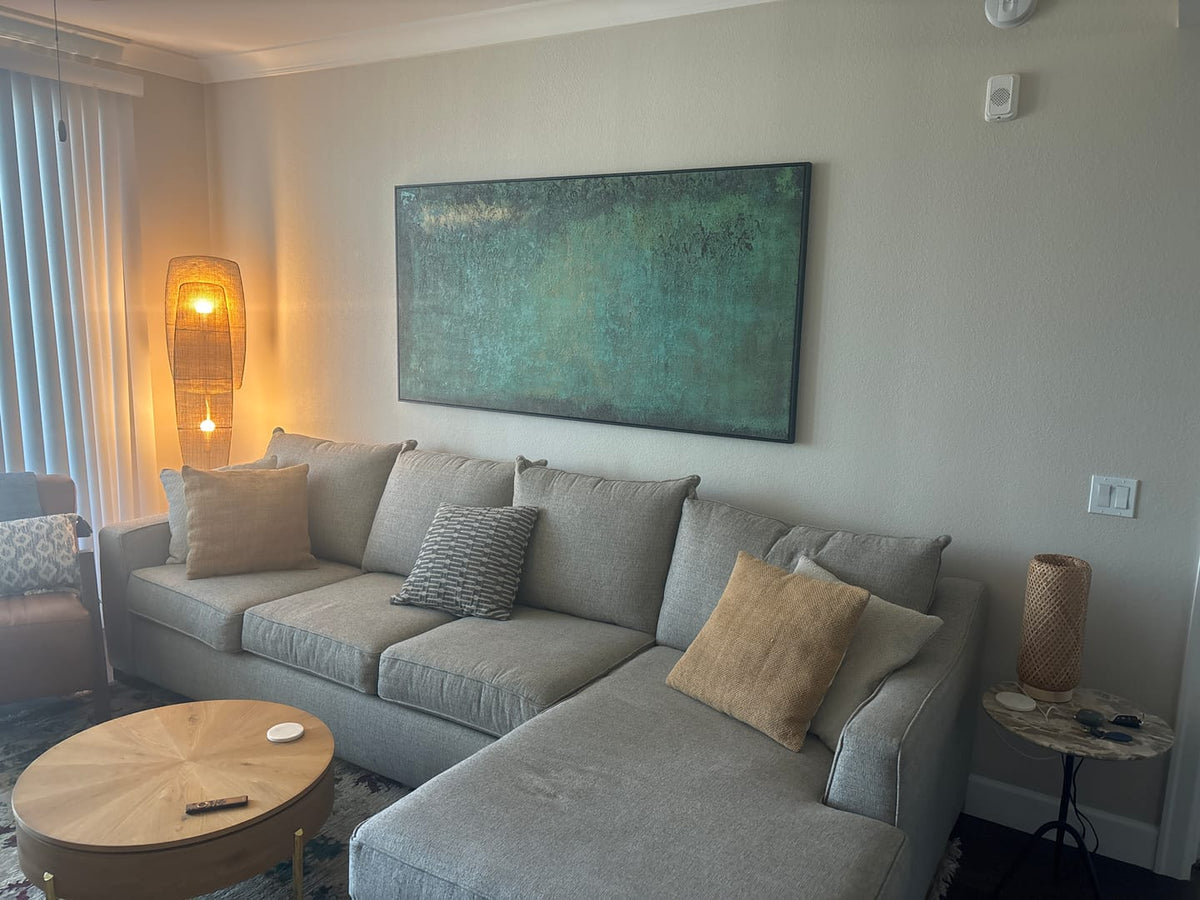 Modern deep green heavy texture distressed painting creating a calm nature inspired aesthetic over a living room sofa.