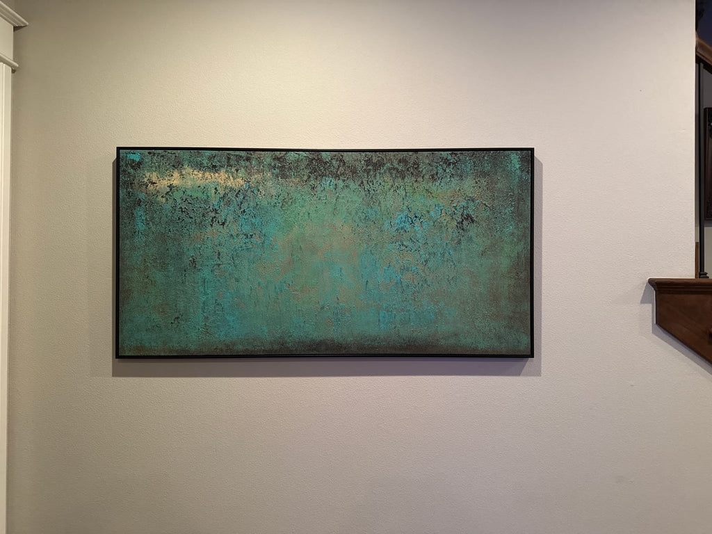 A framed abstract canvas painting featuring textured turquoise, teal, and dark green tones with subtle gold-like highlights, hung on a staircase wall.