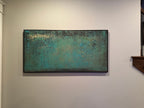 A framed abstract canvas painting featuring textured turquoise, teal, and dark green tones with subtle gold-like highlights, hung on a staircase wall.